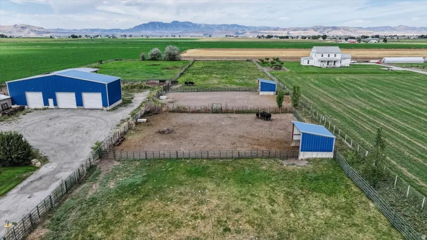 Expansive property featuring a large blue metal outbuilding with three roll-up doors, fenced enclosures, and two blue-roofed shelters