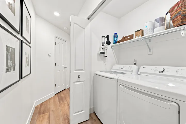 Dedicated laundry area featuring a white shelf for storage, wood-finish flooring, and a paneled door