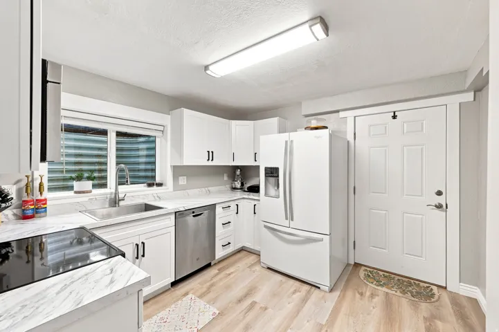 White cabinetry, stainless steel sink, wood-finish flooring, white appliances, and a solid panel door