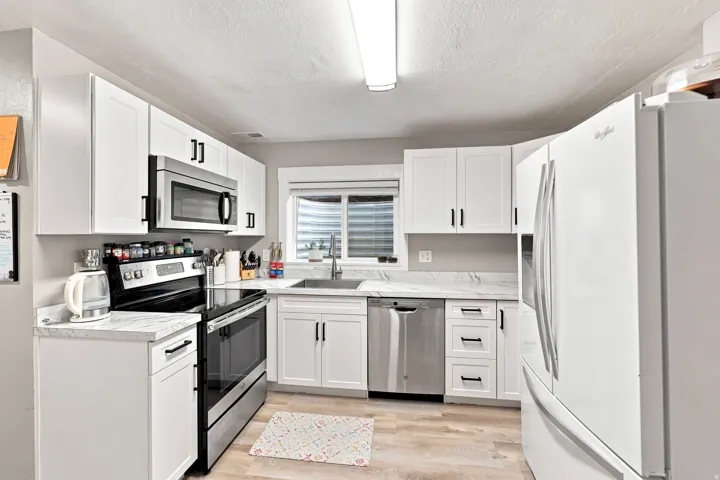 Contemporary kitchen featuring white cabinetry, stainless steel appliances, light-toned countertops, and wood-finish flooring