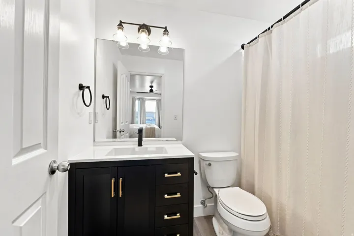 Dark wood-finish vanity with gold-tone hardware, white countertop, rectangular undermount sink, and black-finish faucet