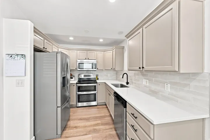 Kitchen featuring light-toned cabinetry, stainless steel appliances, white countertops, and a subway tile backsplash