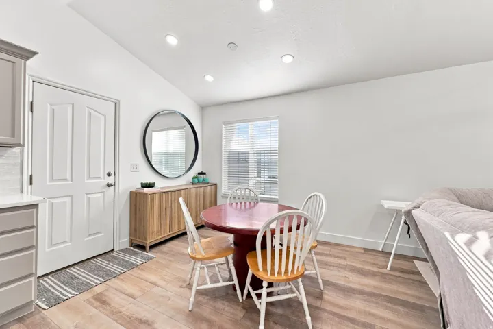 Vaulted ceiling with recessed lighting, wood-finish flooring, white paneled door, and a built-in window with blinds
