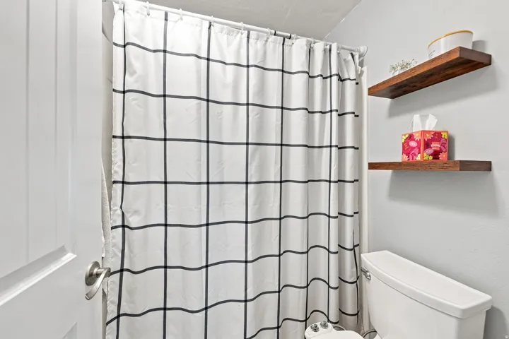 White paneled door with brushed nickel hardware, white toilet, and two wall-mounted wood-finish floating shelves