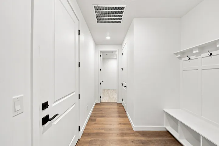 Hallway featuring wood-finish flooring, white panel doors with matte black hardware, recessed lighting, and a built-in bench with coat hooks