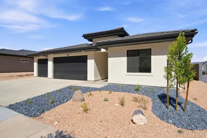 Contemporary stucco exterior with a tiled roof, two-car garage, and desert-style landscaping featuring decorative rocks and plantings