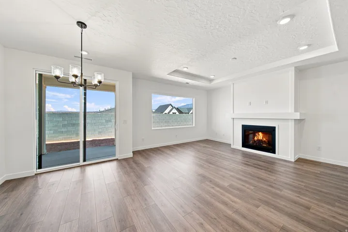 Open-concept living space with wood-finish flooring, a contemporary fireplace, and a tray ceiling with recessed lighting