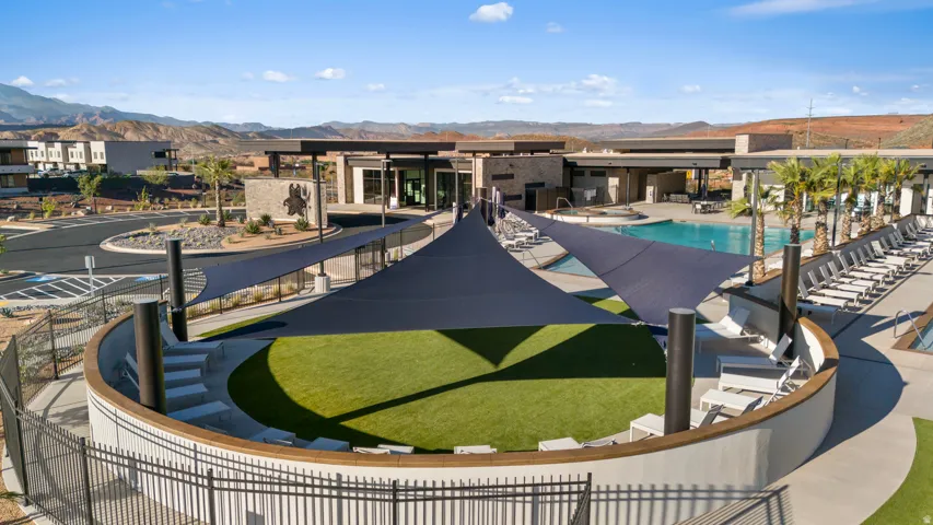 Outdoor amphitheater with artificial turf, multiple shade structures, and an expansive pool area with integrated spa