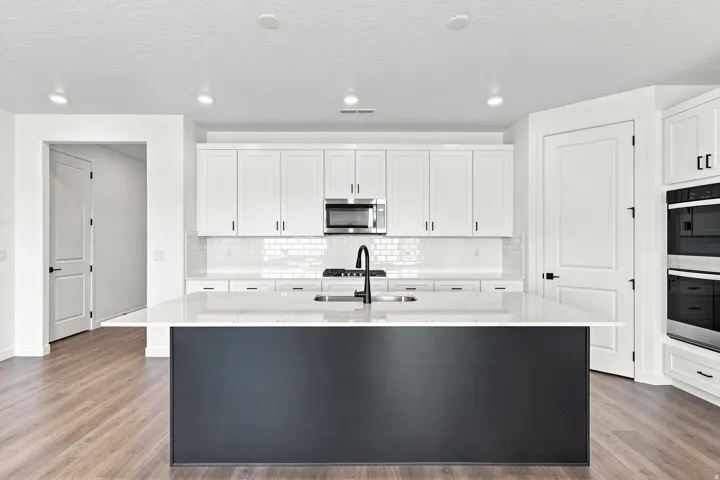 White shaker cabinetry, stainless steel appliances, a center island with a sink, white subway tile backsplash, and wood-finish flooring