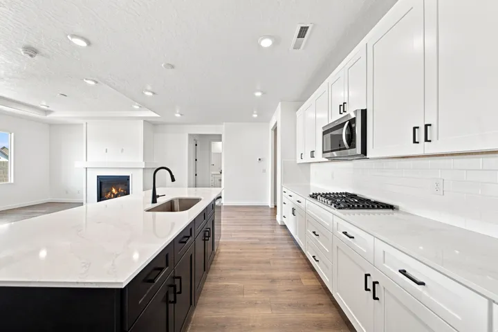 White shaker-style cabinetry with black hardware, white subway tile backsplash, stainless steel gas range, and a large kitchen island with an undermount sink