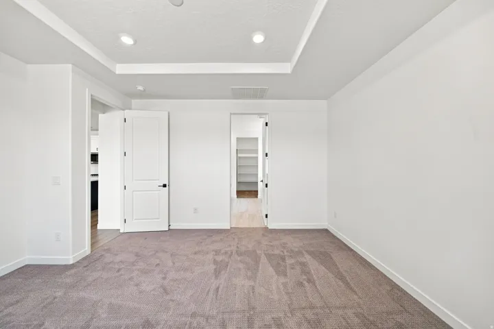 Recessed lighting, tray ceiling, neutral-toned carpet, white walls, and contemporary doors