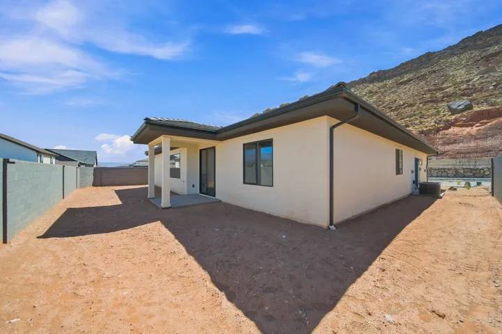 Stucco exterior with dark trim and a covered patio, featuring a dark tiled roof and an attached rain gutter system