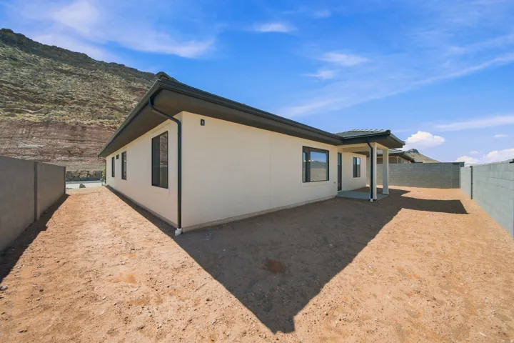 Stucco exterior with a covered patio, dark framed windows, and a tiled roof, set against a mountainous backdrop