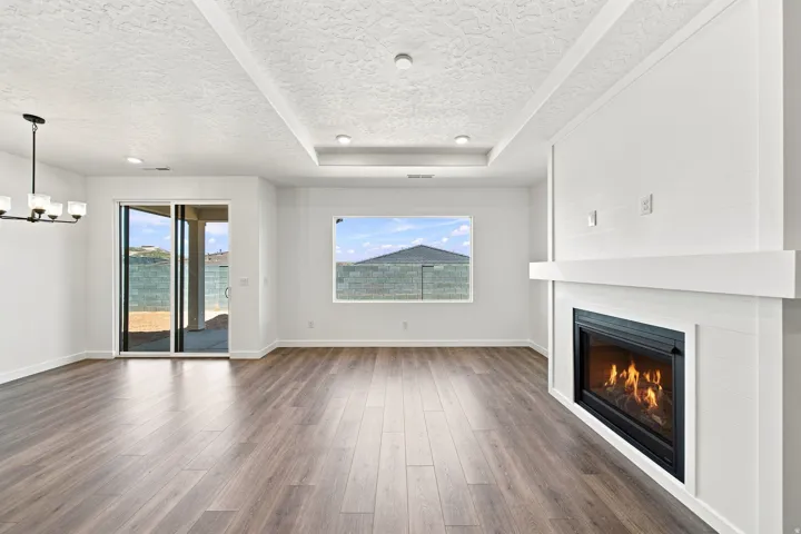 Wood-finish flooring throughout, tray ceiling with recessed lighting, integrated electric fireplace with mantel, sliding glass door, and chandelier
