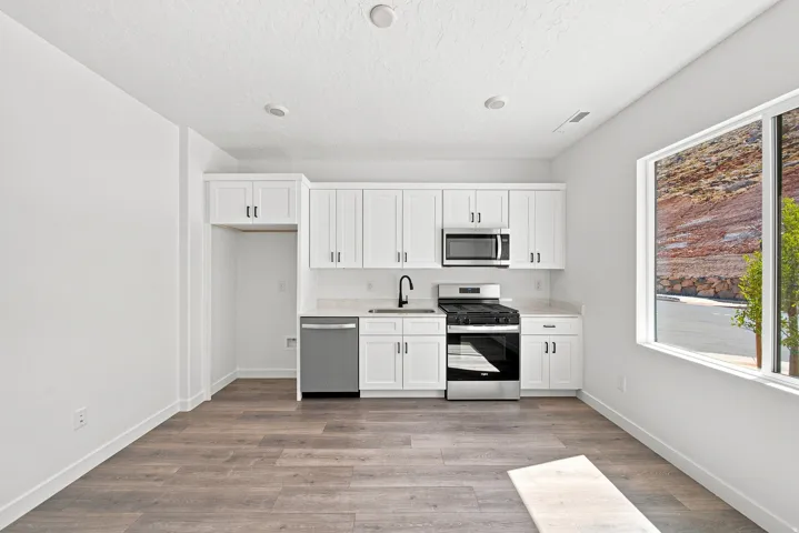 Casita KitchenContemporary kitchen featuring white cabinetry, stainless steel appliances, wood-finish flooring, recessed lighting, and a large window