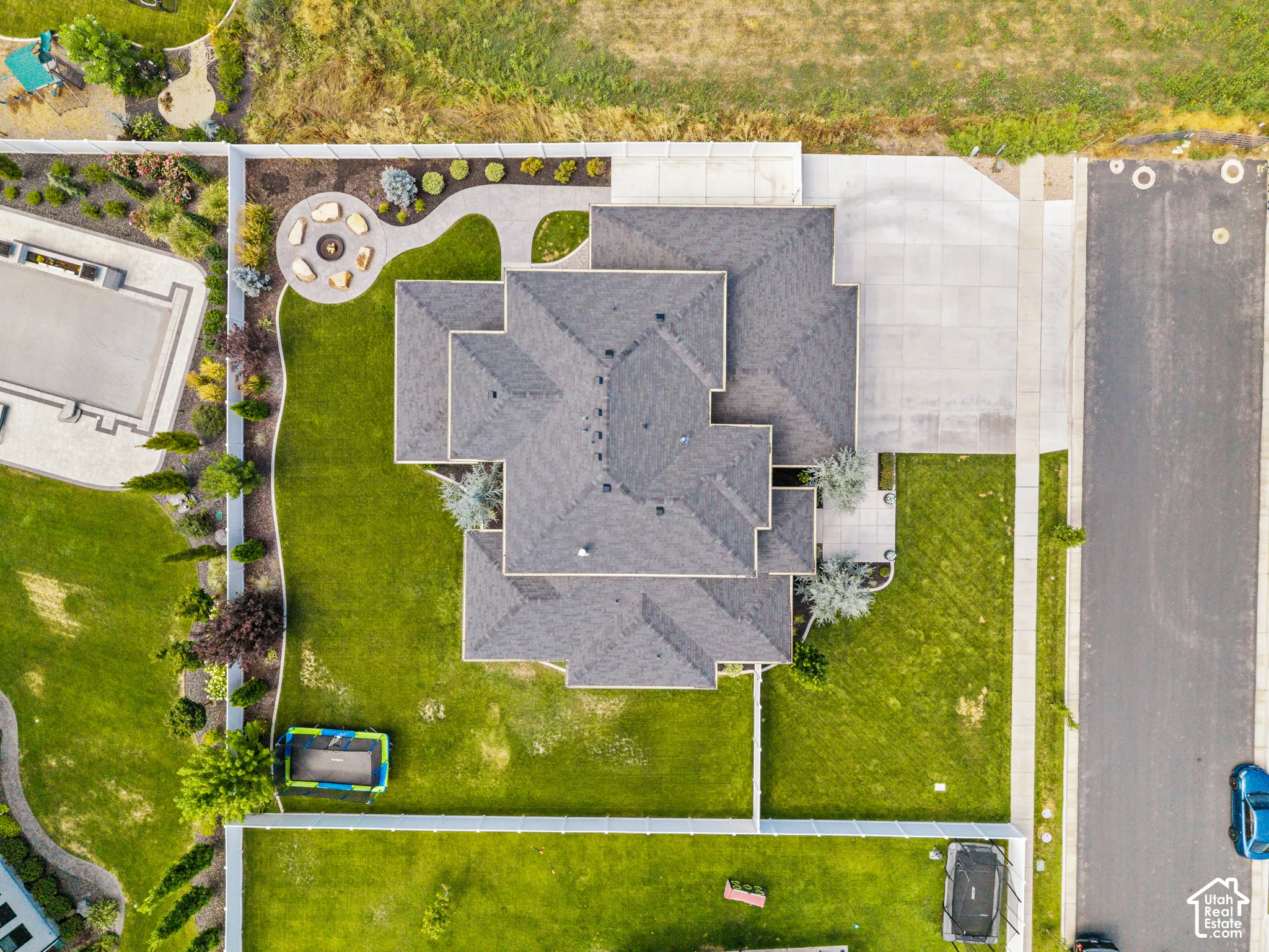 Aerial view showcasing a substantial residence with a multi-pitched asphalt shingle roof, expansive manicured lawn with mature landscaping, circular driveway with concrete paving, and adjoining structures including a detached garage