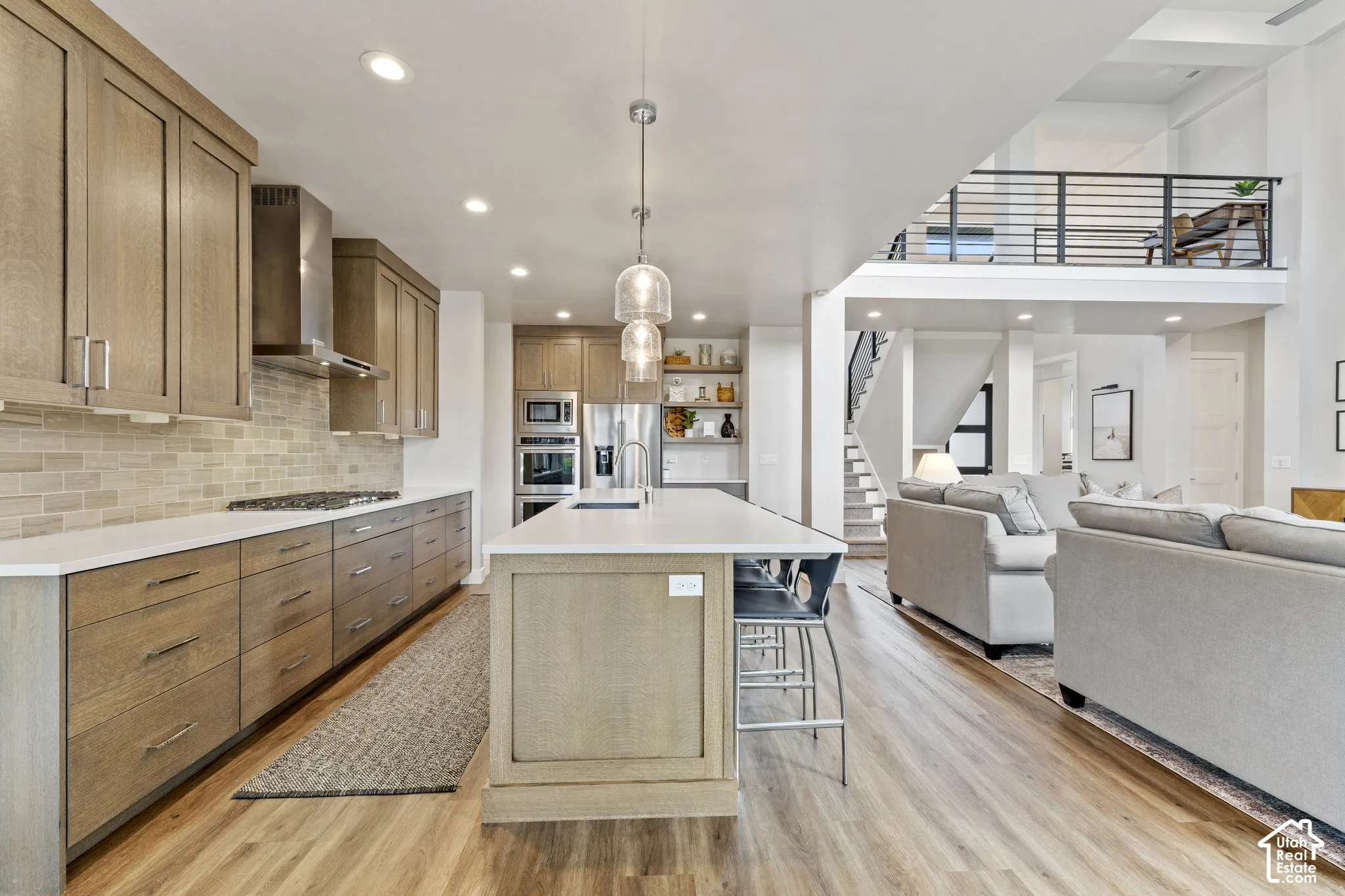 Open-concept living space with wood-finish flooring, a kitchen island, and a second-level balcony