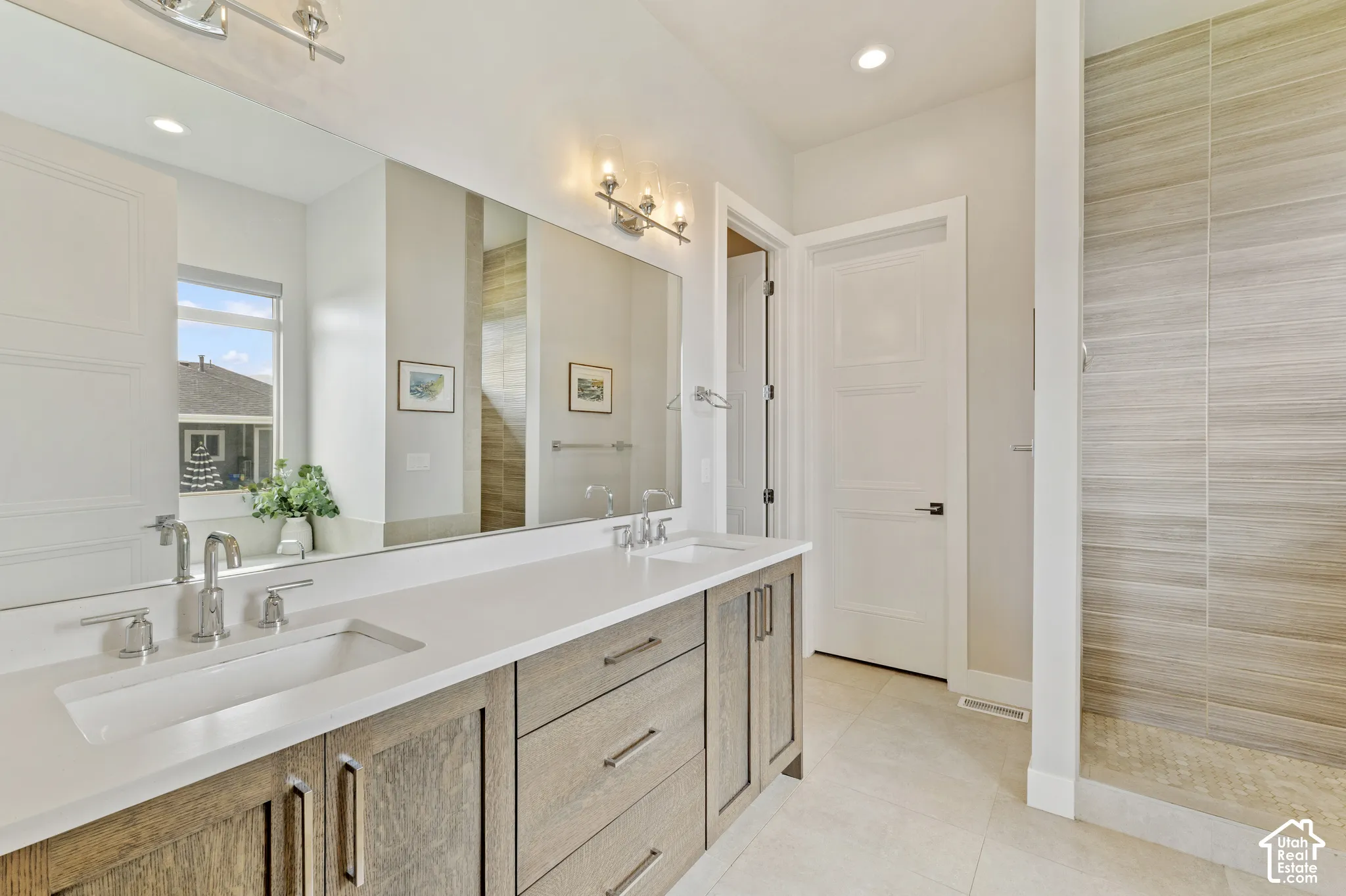 Spa-inspired primary bathroom showcasing a lengthy dual-sink vanity with wood-finish cabinetry, white quartz countertops, and polished nickel fixtures