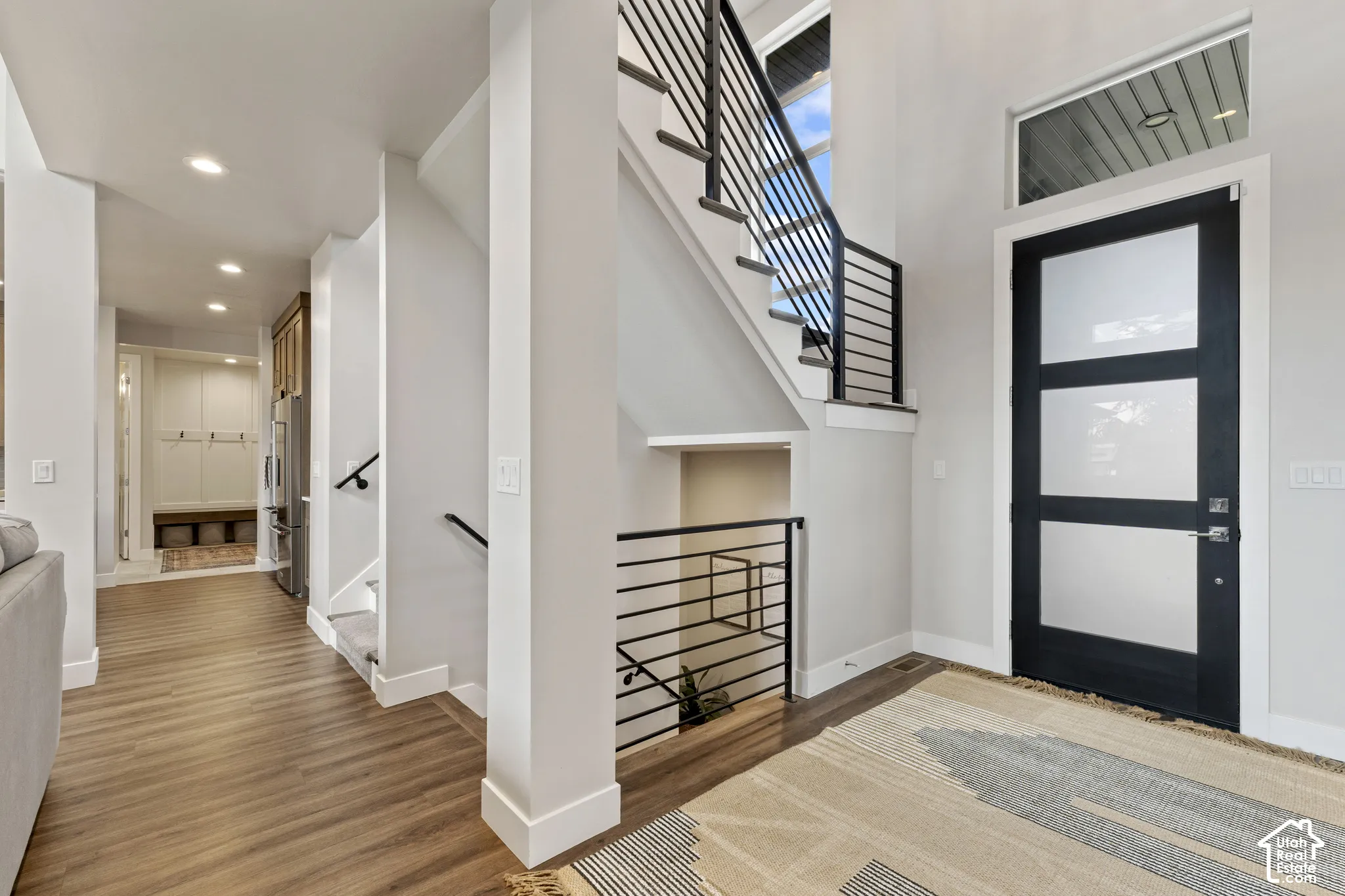 Modern foyer featuring warm wood-finish flooring, white painted walls, and a striking black-framed glass door