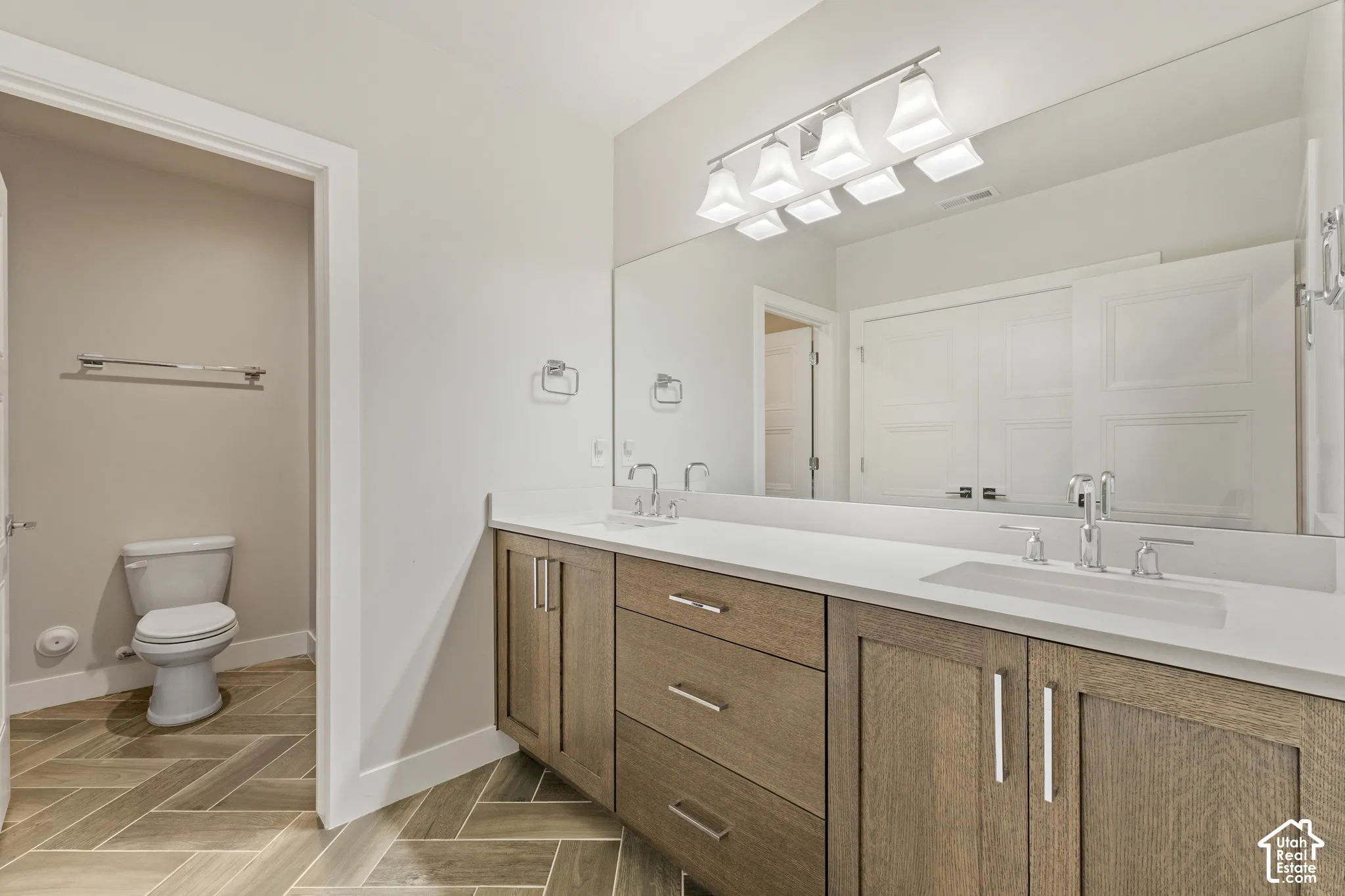 Spa-inspired primary bathroom featuring a wood-finish vanity with dual sinks, white quartz countertop, polished chrome fixtures, and an extensive mirror with integrated lighting