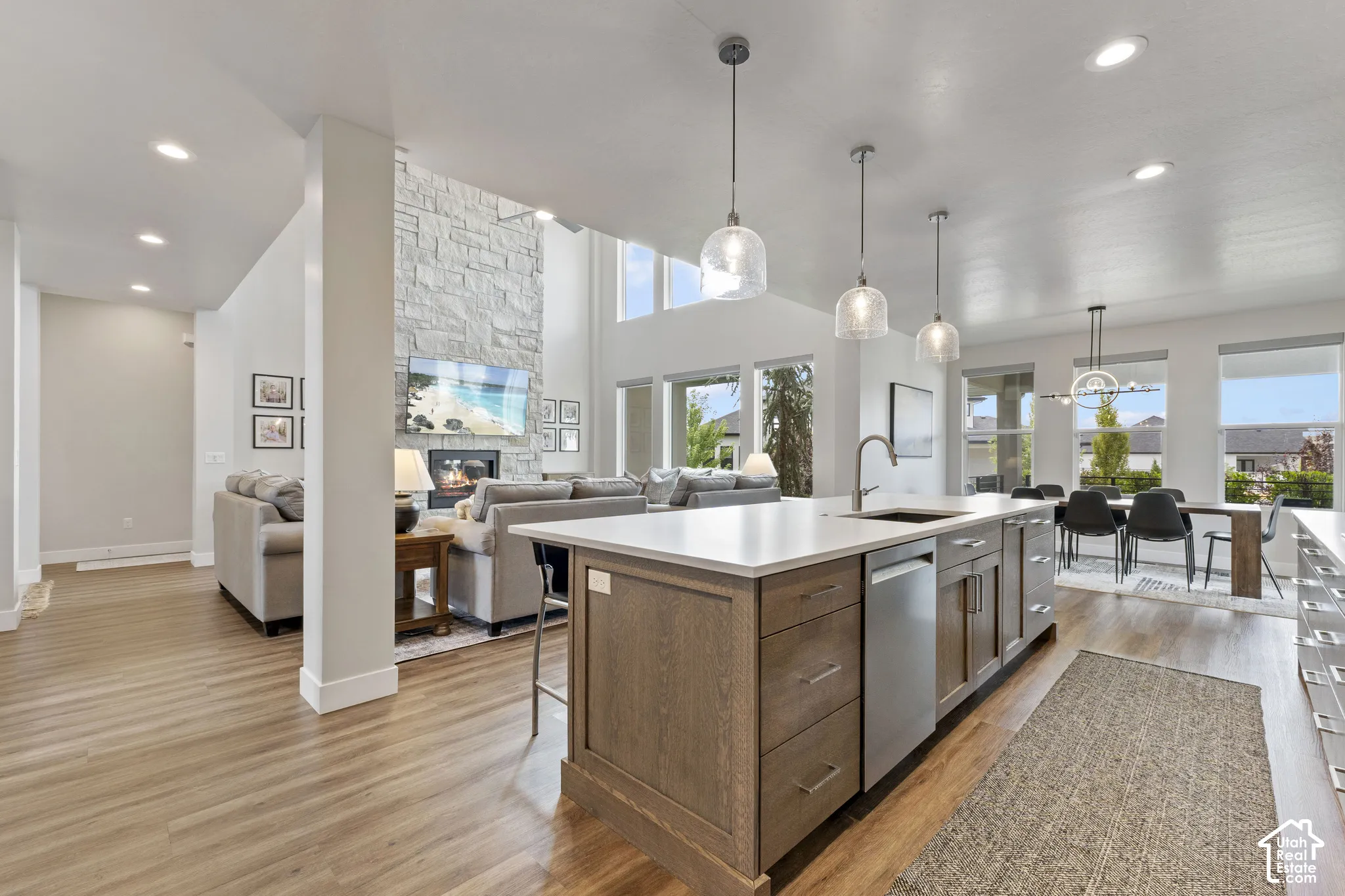 Open-concept kitchen and living area featuring a large wood-finish island with stainless steel appliances, white quartz countertops, pendant lighting, soaring ceilings with skylights, hardwood flooring, and expansive windows framing panoramic landscape vi