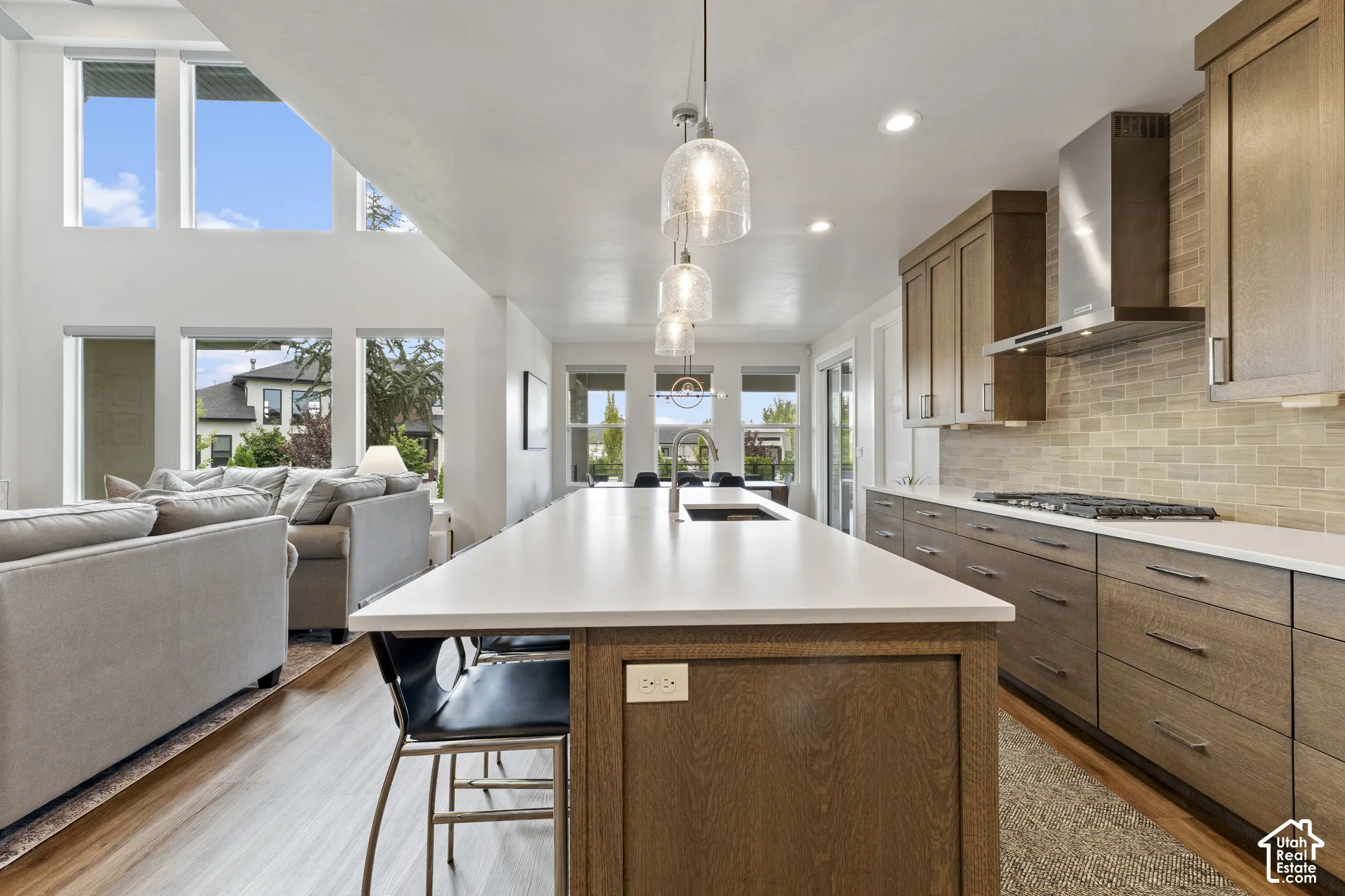 Open-concept kitchen featuring an expansive center island, integrated gas range with stainless steel hood, wood-finish cabinetry, and a tile backsplash