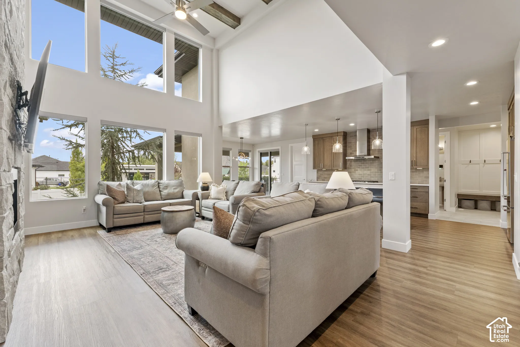 Expansive living area with high ceilings, large windows, wood-finish flooring, and a stone-clad fireplace