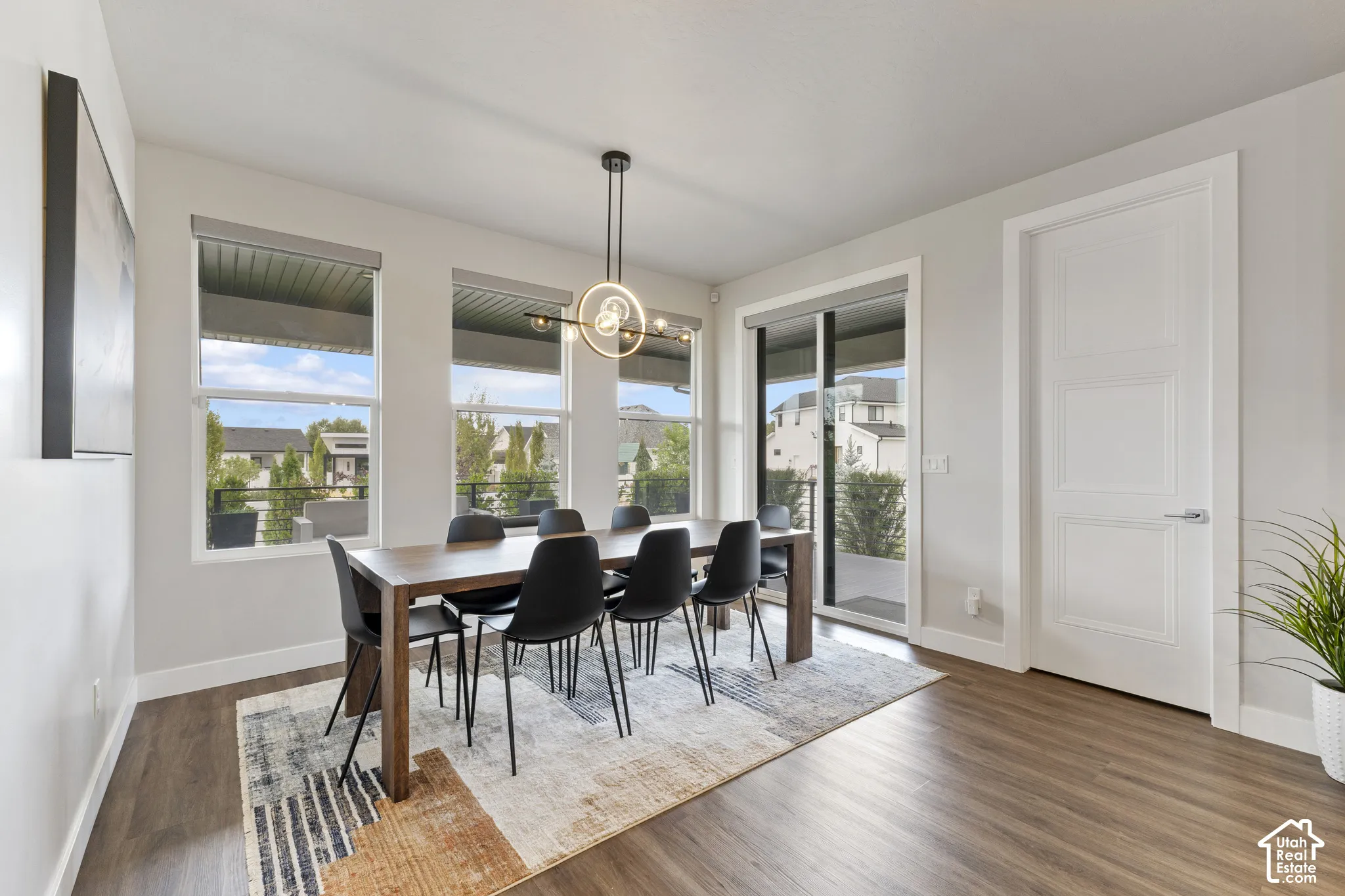 Wood-finish flooring with a modern linear chandelier, multiple windows, and a sliding glass door