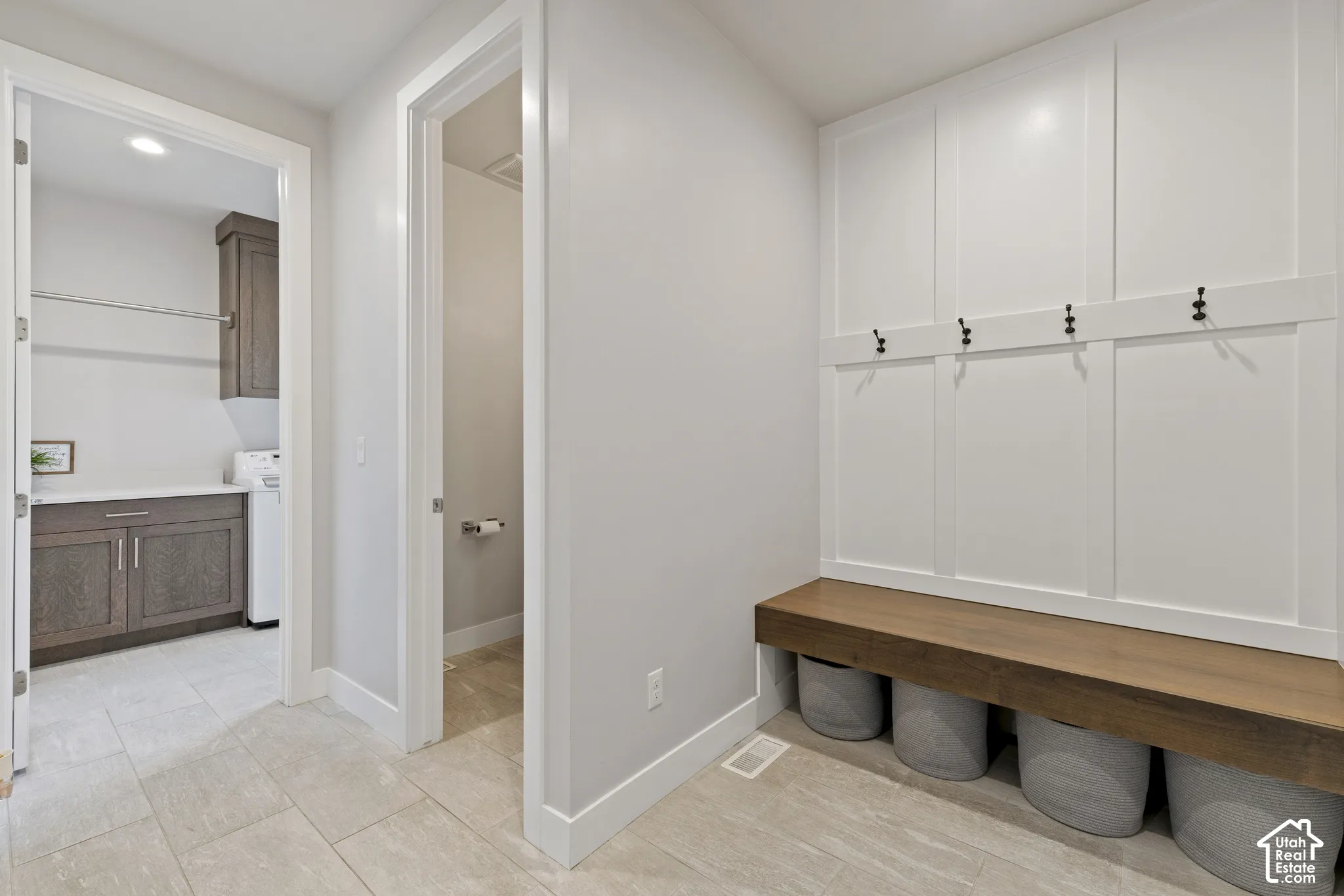 Dedicated mudroom and laundry space featuring built-in cabinetry with four hooks for organized storage, wood-finish bench seating with integrated cubbies for shoes and accessories, and direct access to the primary bathroom