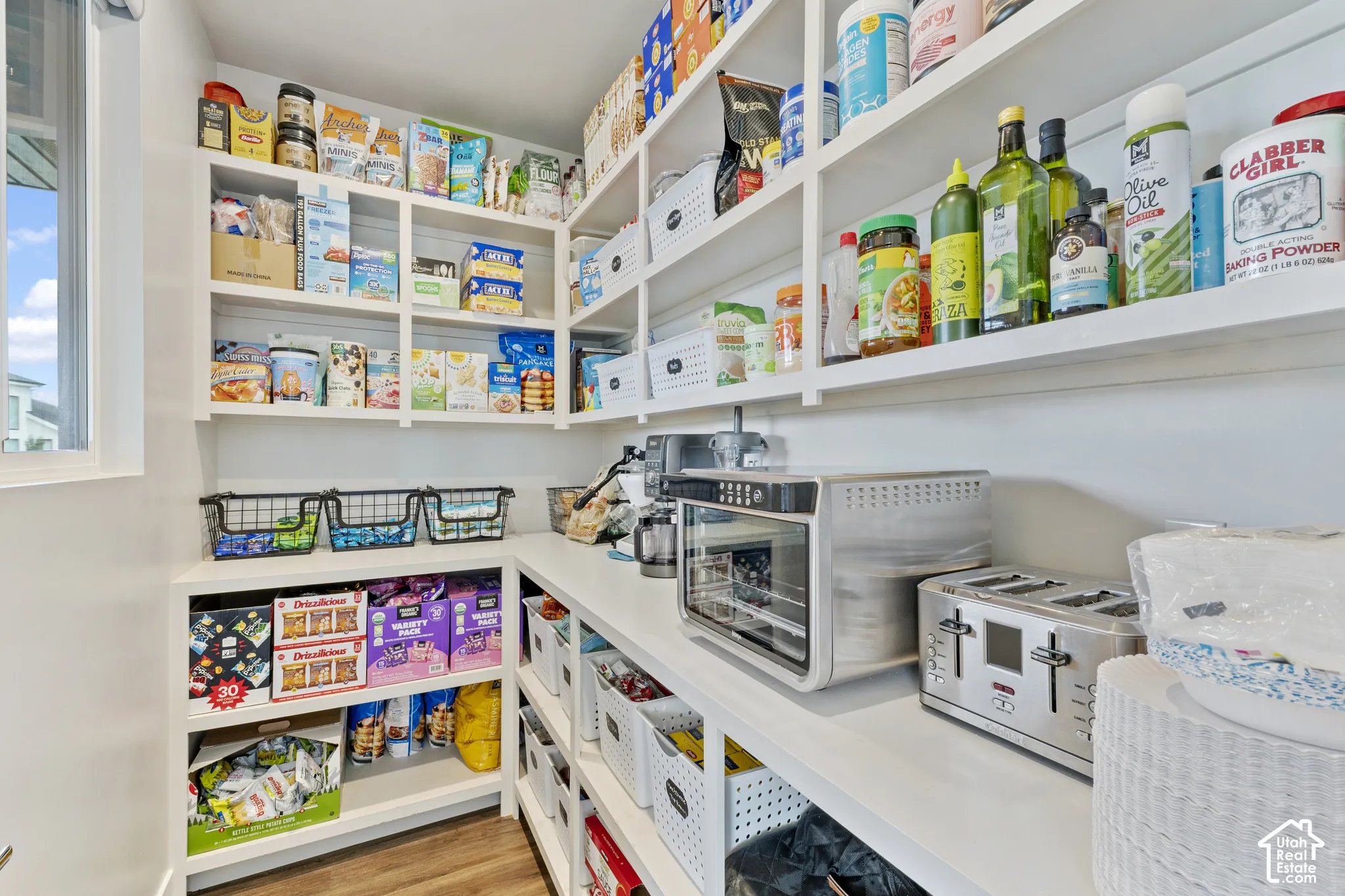 Organized pantry featuring expansive built-in shelving with multiple tiers for dry goods and pantry staples, wire storage baskets for easy access, and dedicated counter space with small appliances