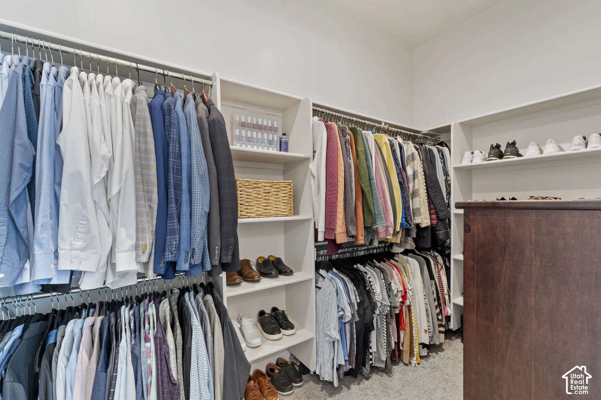 Spacious walk-in closet featuring dual clothing rods with extensive hanging capacity, built-in shelving with cubbies and compartments for organized storage, wood-finish flooring, and recessed lighting throughout