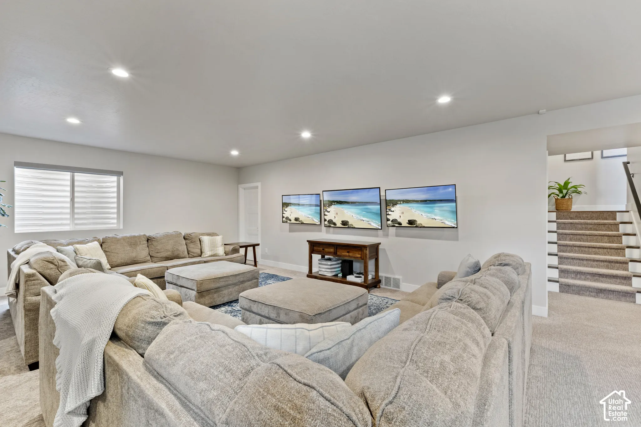 Expansive rec room featuring recessed ceiling lighting, neutral wall finishes, and multiple seating areas anchored by a wood-finish media console