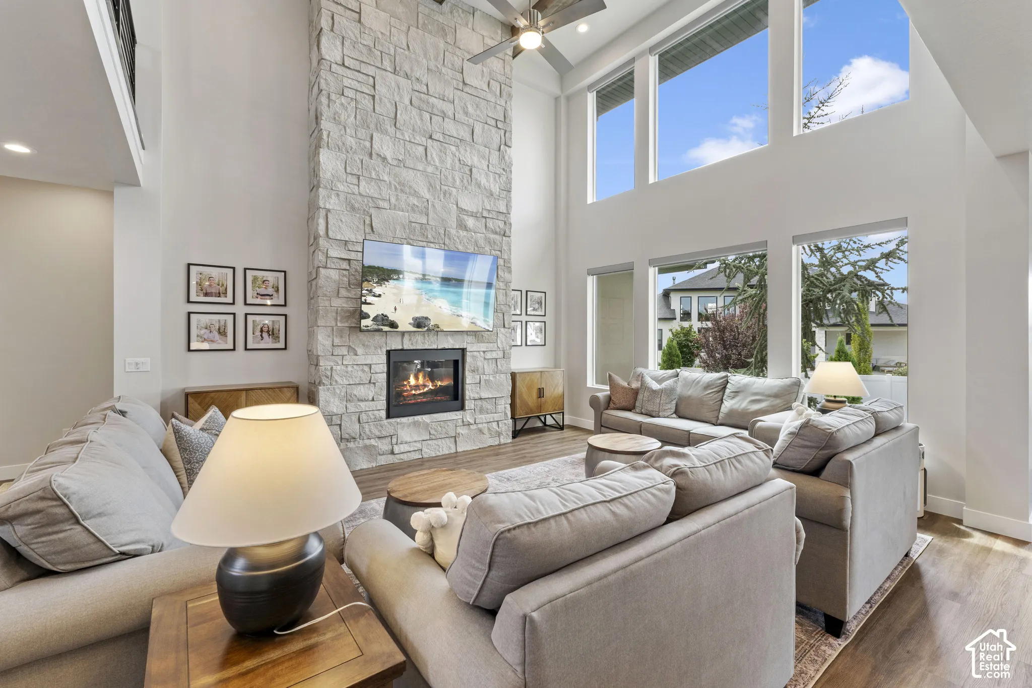 Soaring two-story living room anchored by a linear gas fireplace with stacked stone surround and mounted television