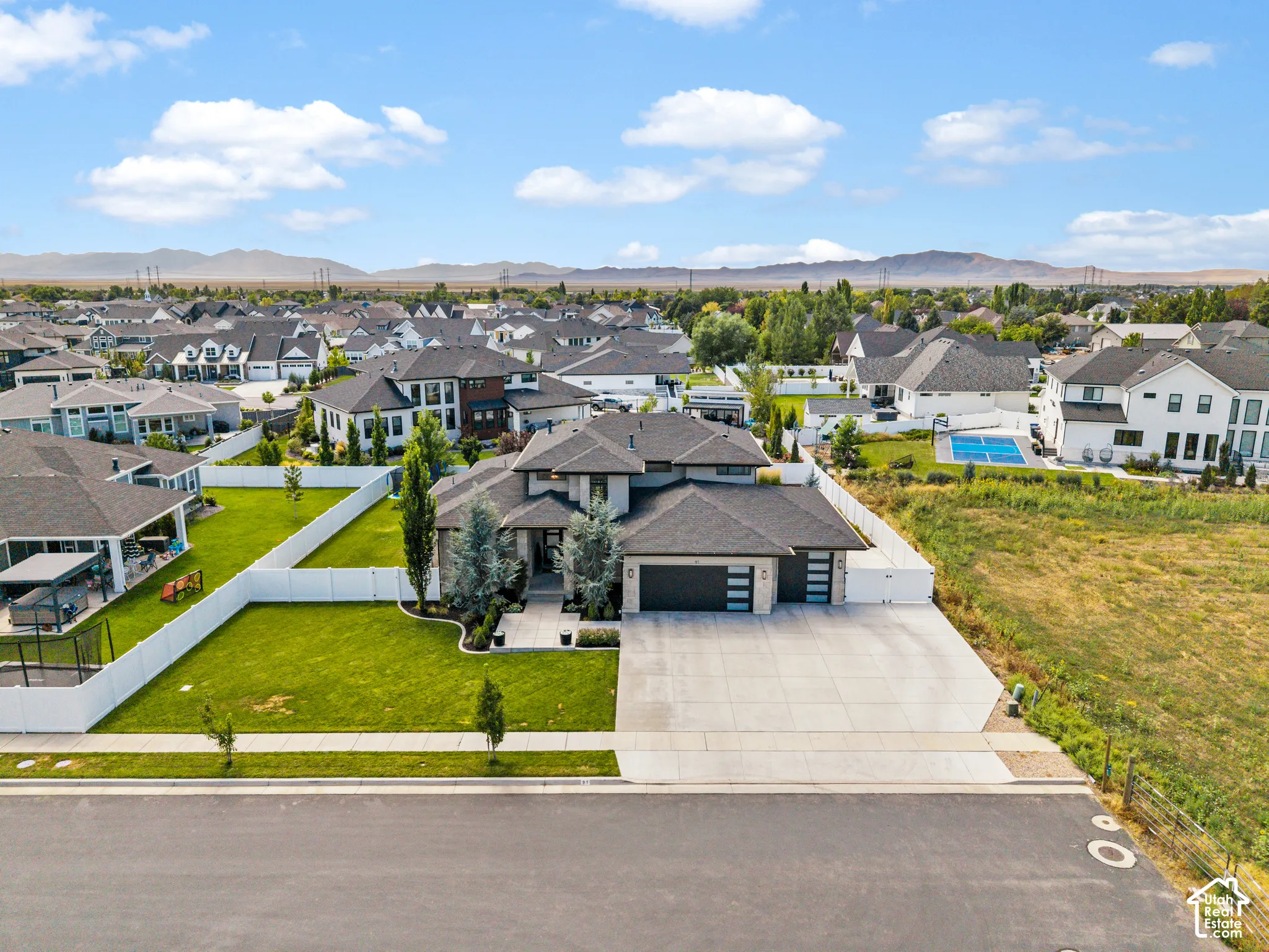 Modern residence showcasing a striking contemporary exterior with dark architectural accents, expansive concrete driveway, manicured lawn with mature landscaping, and a serene mountain backdrop visible across the established residential community