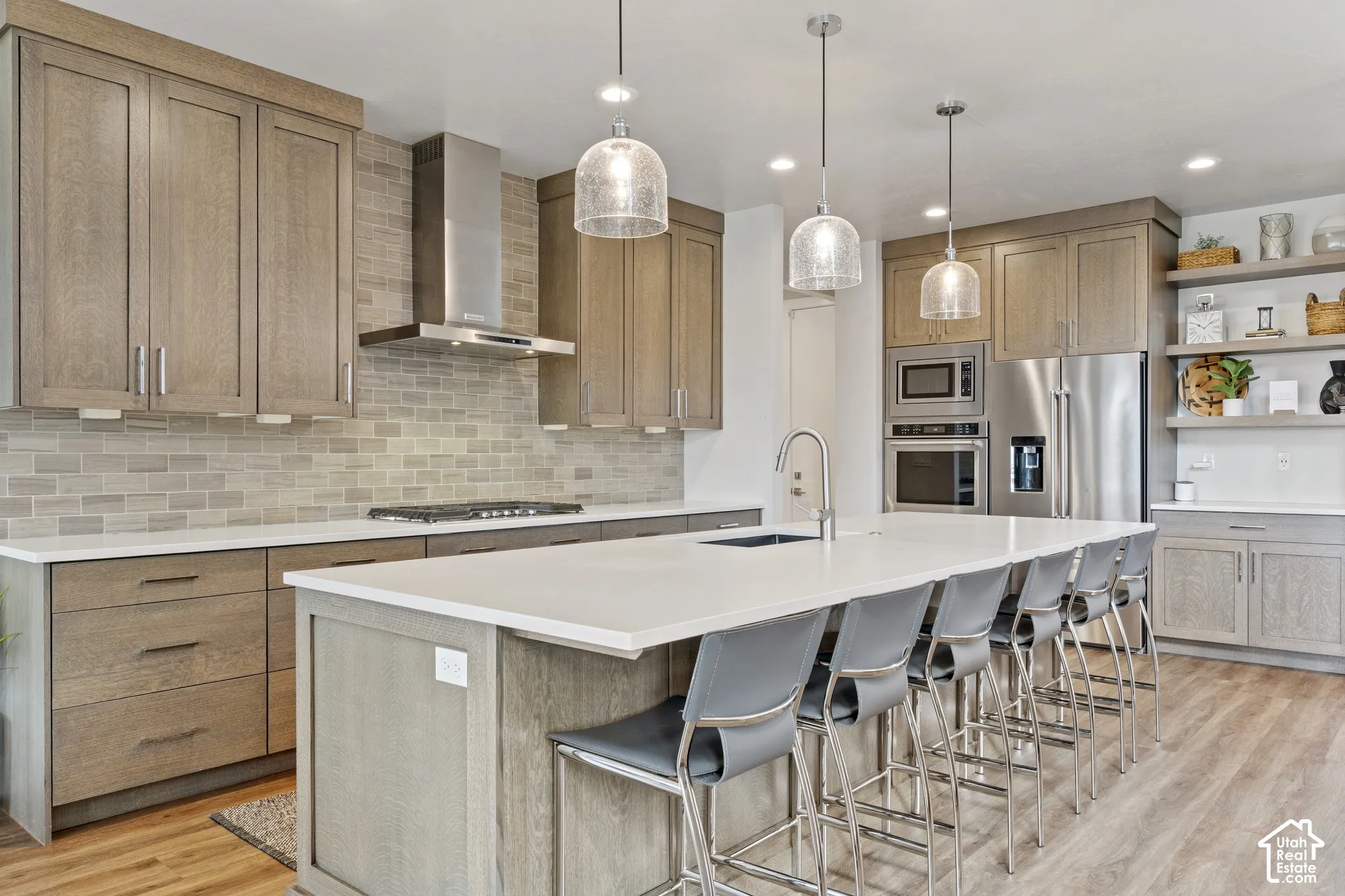 Spacious kitchen featuring an expansive island with seating, stainless steel appliances, wood-finish cabinetry, white countertops, and wood-finish flooring
