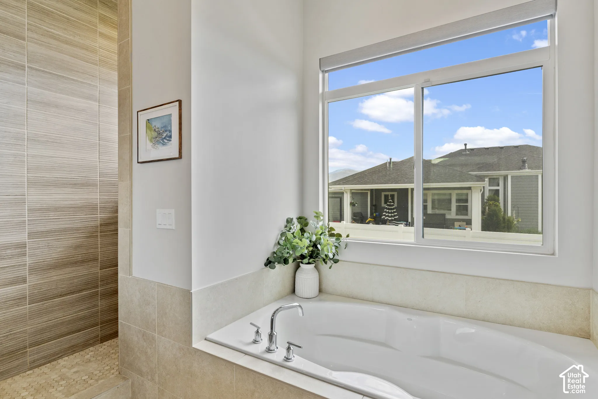 Spa-inspired primary bathroom featuring a soaking tub with deck-mounted faucet, tile surround, and wood-finish accents