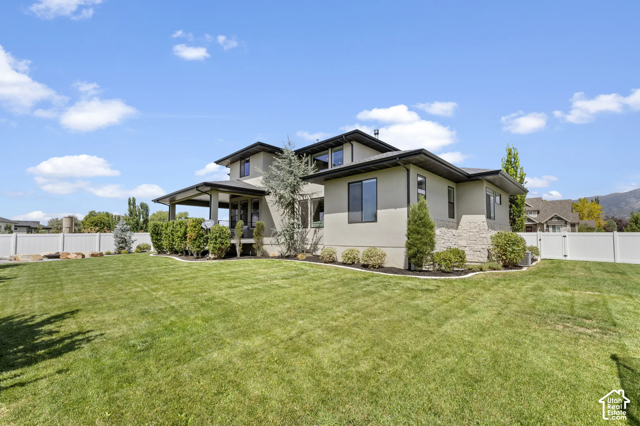 Expansive lawn with a white privacy fence, covered patio, and stucco exterior with stone accents