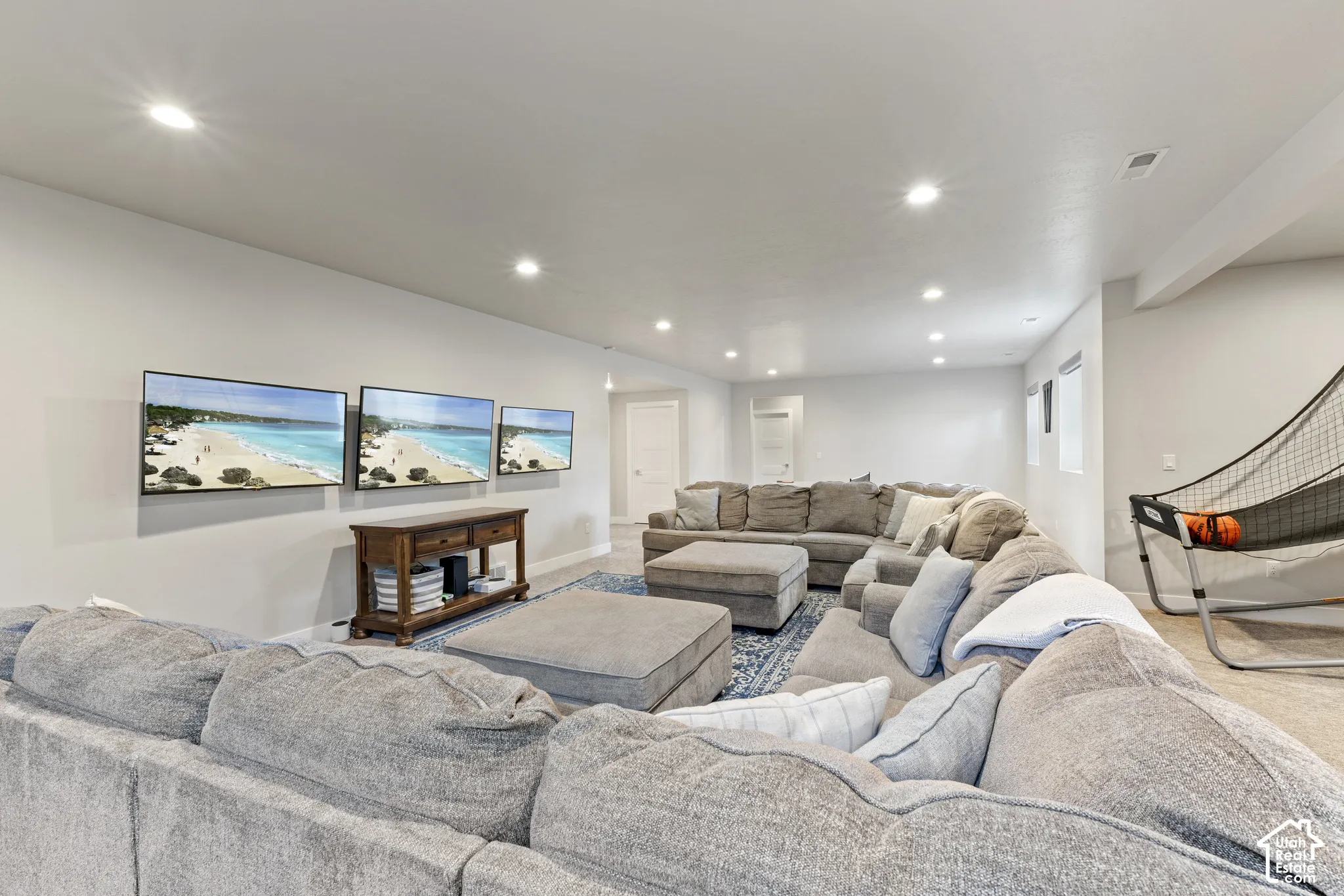 Expansive recreation room featuring multiple wall-mounted flat-screen displays, recessed ceiling lighting, and generous seating areas with neutral upholstery