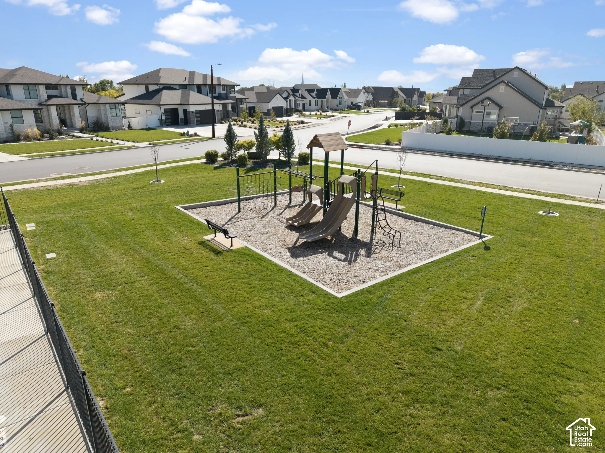 Spacious green space featuring a playground with slides and climbing structures, surrounded by residential streetscapes