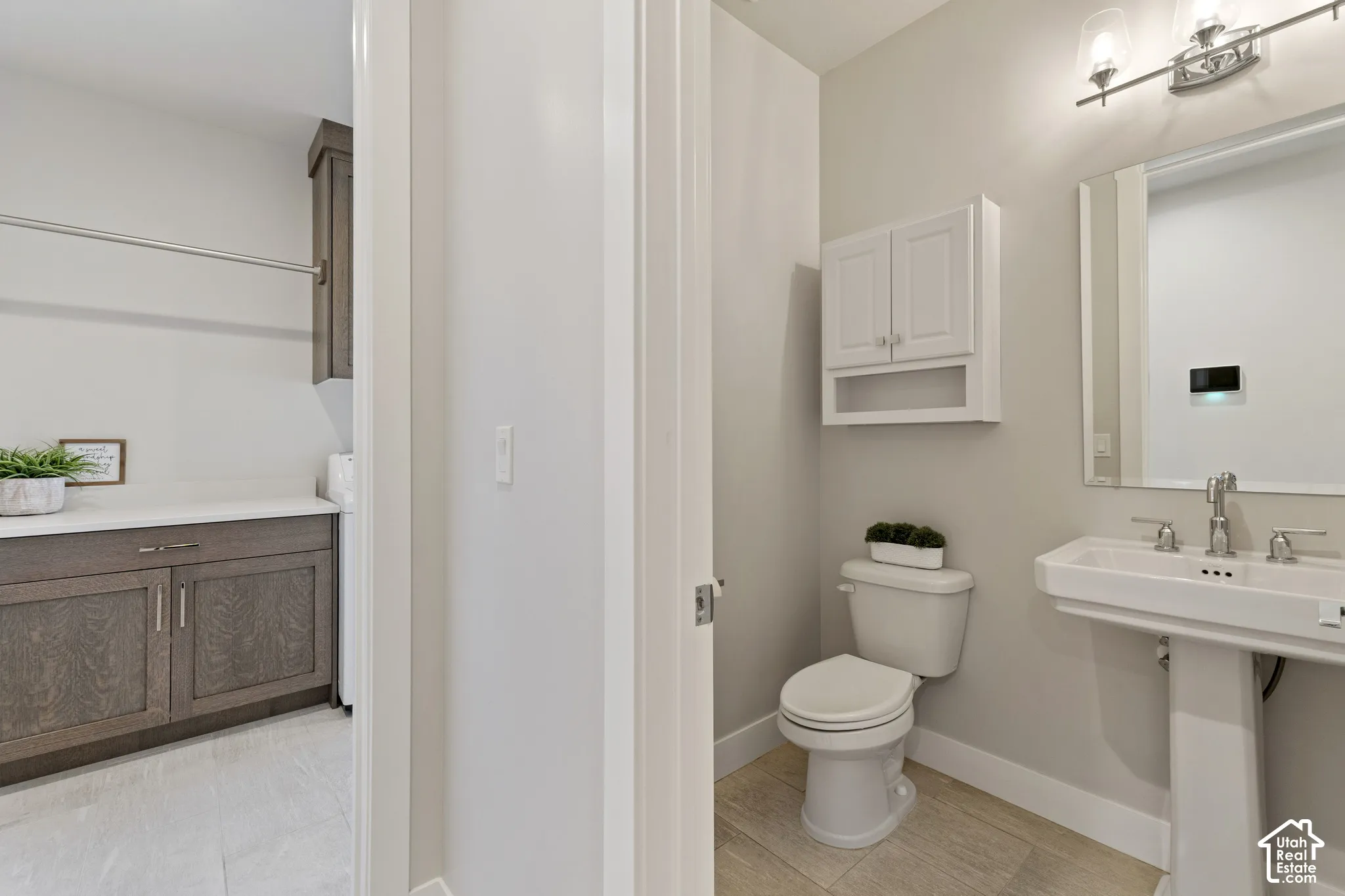 Dual-sink pedestal vanity with polished chrome fixtures and framed mirror, complemented by wood-finish flooring, white subway tile backsplash, and soft neutral wall finishes