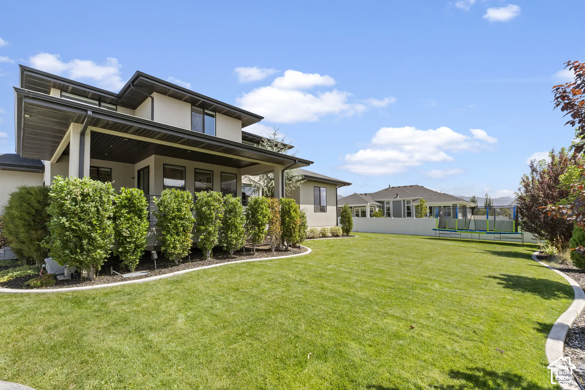 Expansive backyard featuring a manicured lawn, established landscaping, and a covered patio