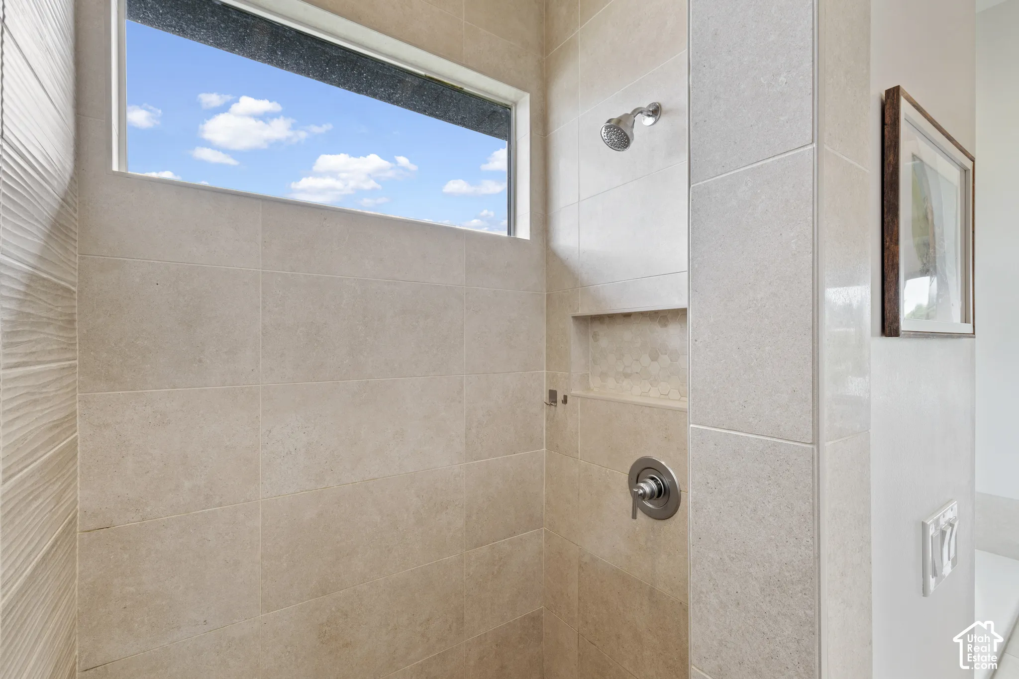 Spa-inspired ensuite bathroom featuring large-format neutral tile walls, a walk-in shower with dual showerheads, chrome fixtures, and a transom window flooding the space with natural light