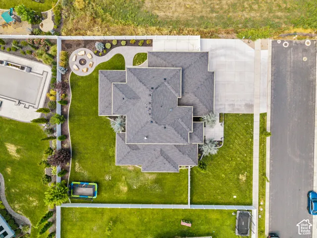 Aerial view showcasing a substantial residence with a multi-pitched asphalt shingle roof, expansive manicured lawn with mature landscaping, circular driveway with concrete paving, and adjoining structures including a detached garage