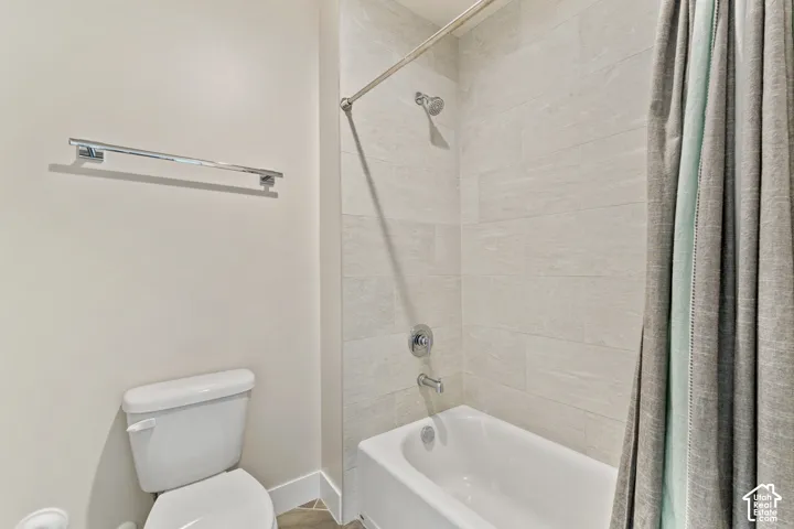 Clean and functional bathroom featuring a white porcelain toilet, alcove bathtub with tile surround, chrome showerhead and trim, and a fabric shower curtain