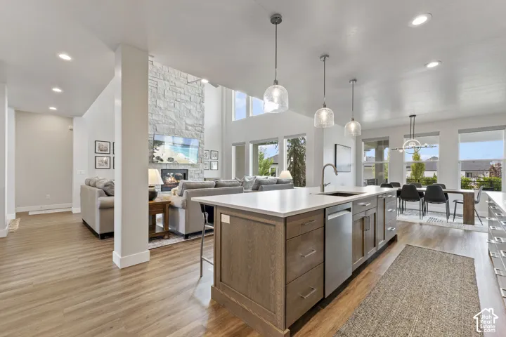 Open-concept kitchen and living area featuring a large wood-finish island with stainless steel appliances, white quartz countertops, pendant lighting, soaring ceilings with skylights, hardwood flooring, and expansive windows framing panoramic landscape vi