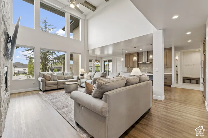 Expansive living area with high ceilings, large windows, wood-finish flooring, and a stone-clad fireplace