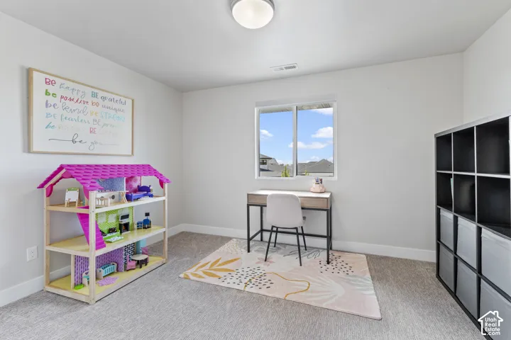 Bright, multi-purpose room featuring large windows with natural light, neutral carpeting, built-in black storage cubbies, and a dedicated work area with desk and chair