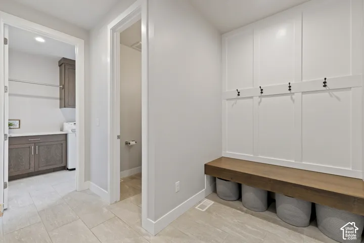 Dedicated mudroom and laundry space featuring built-in cabinetry with four hooks for organized storage, wood-finish bench seating with integrated cubbies for shoes and accessories, and direct access to the primary bathroom