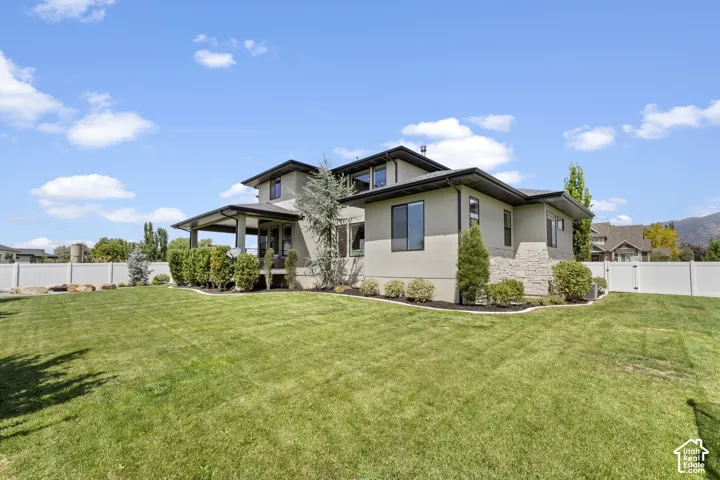 Expansive lawn with a white privacy fence, covered patio, and stucco exterior with stone accents