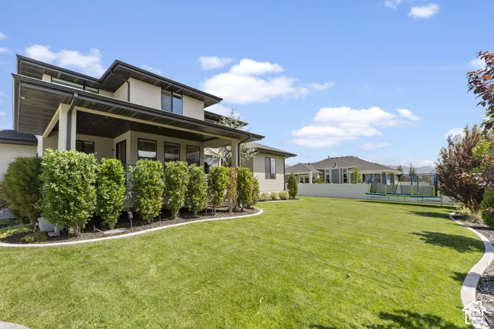 Expansive backyard featuring a manicured lawn, established landscaping, and a covered patio